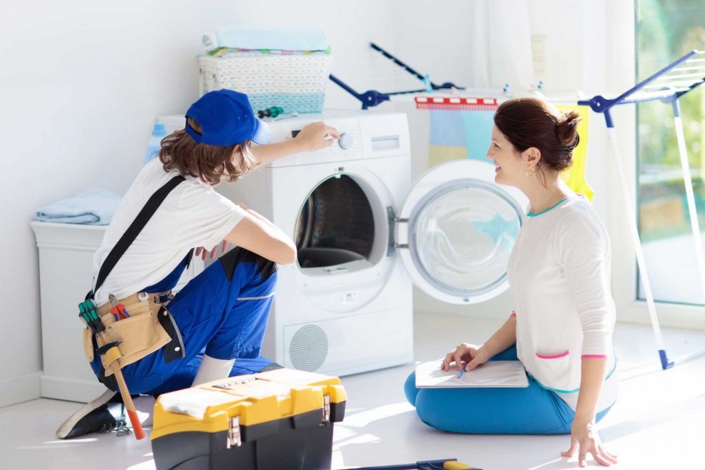 a technician repairing a washer while woman is watching - appliance repair service Roswell